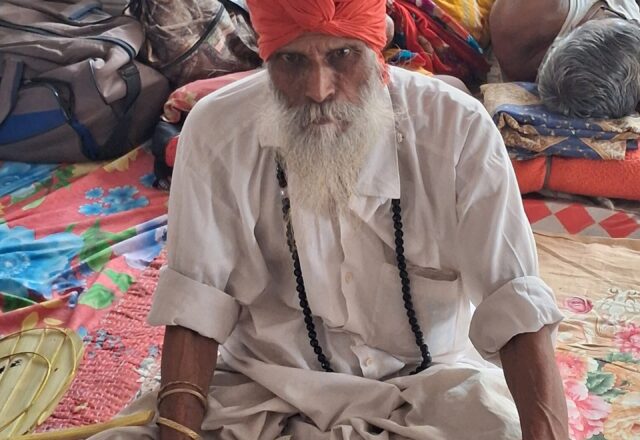 Baul elder with a white beard, orange turban and prayer beads at Lalon Akhra