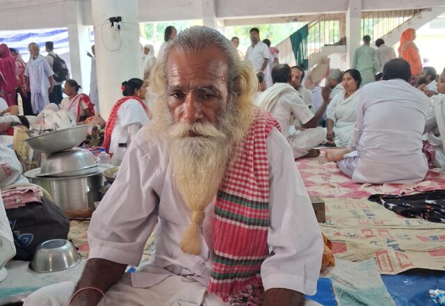 Baul elder in white and a red gamchha seated in the hall at Lalon Akhra