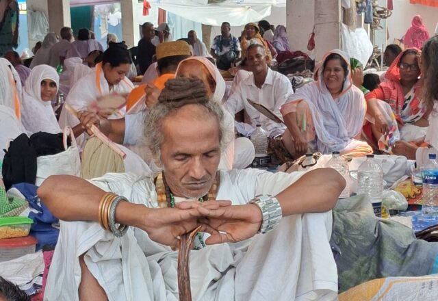 Baul elder in white seated with his staff among pilgrims at Lalon Akhra
