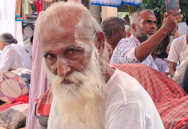 Elderly baul with a white beard sitting among pilgrims at the Lalon Mela